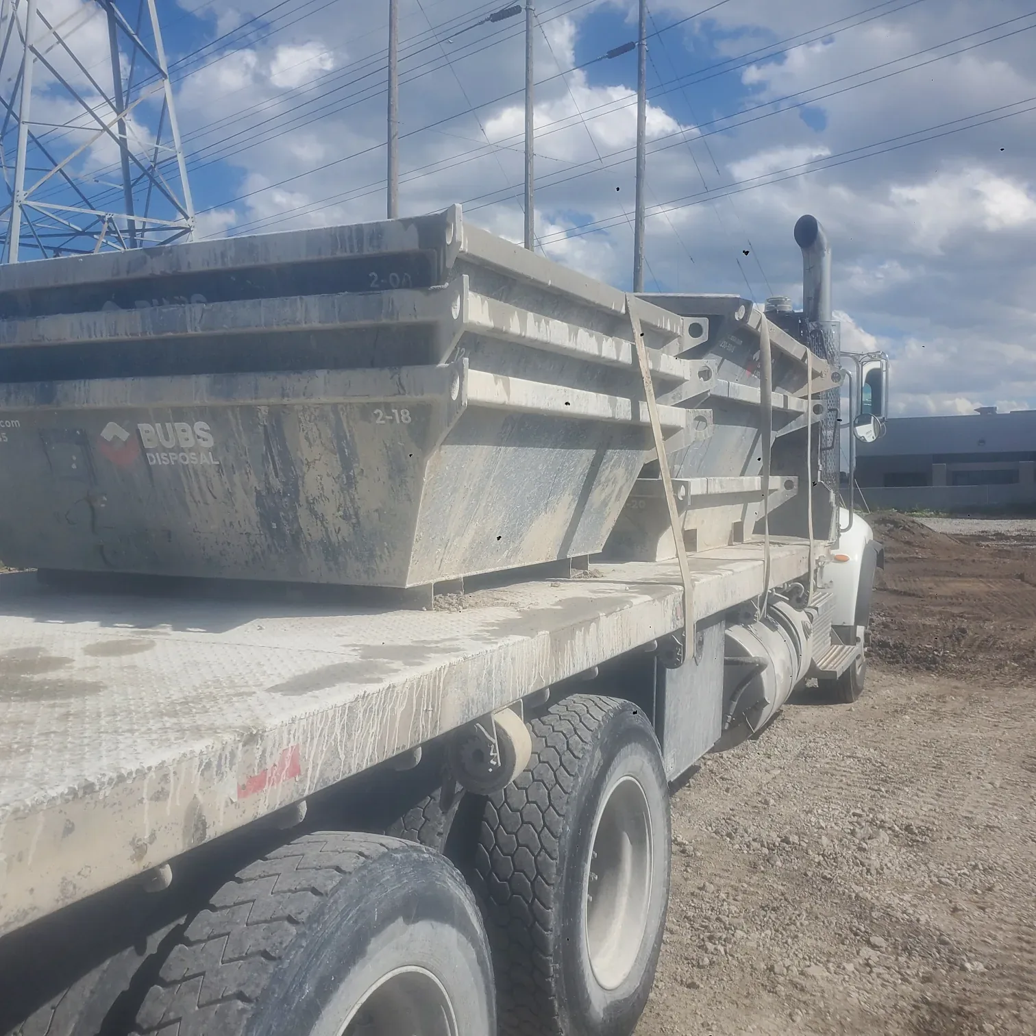 Bubs Disposal washout bin being crane-lowered onto a flatbed truck at a construction site