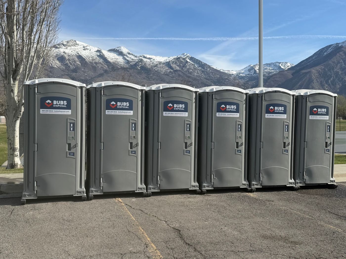Six Bubs porta potties lined up with snowy mountains behind