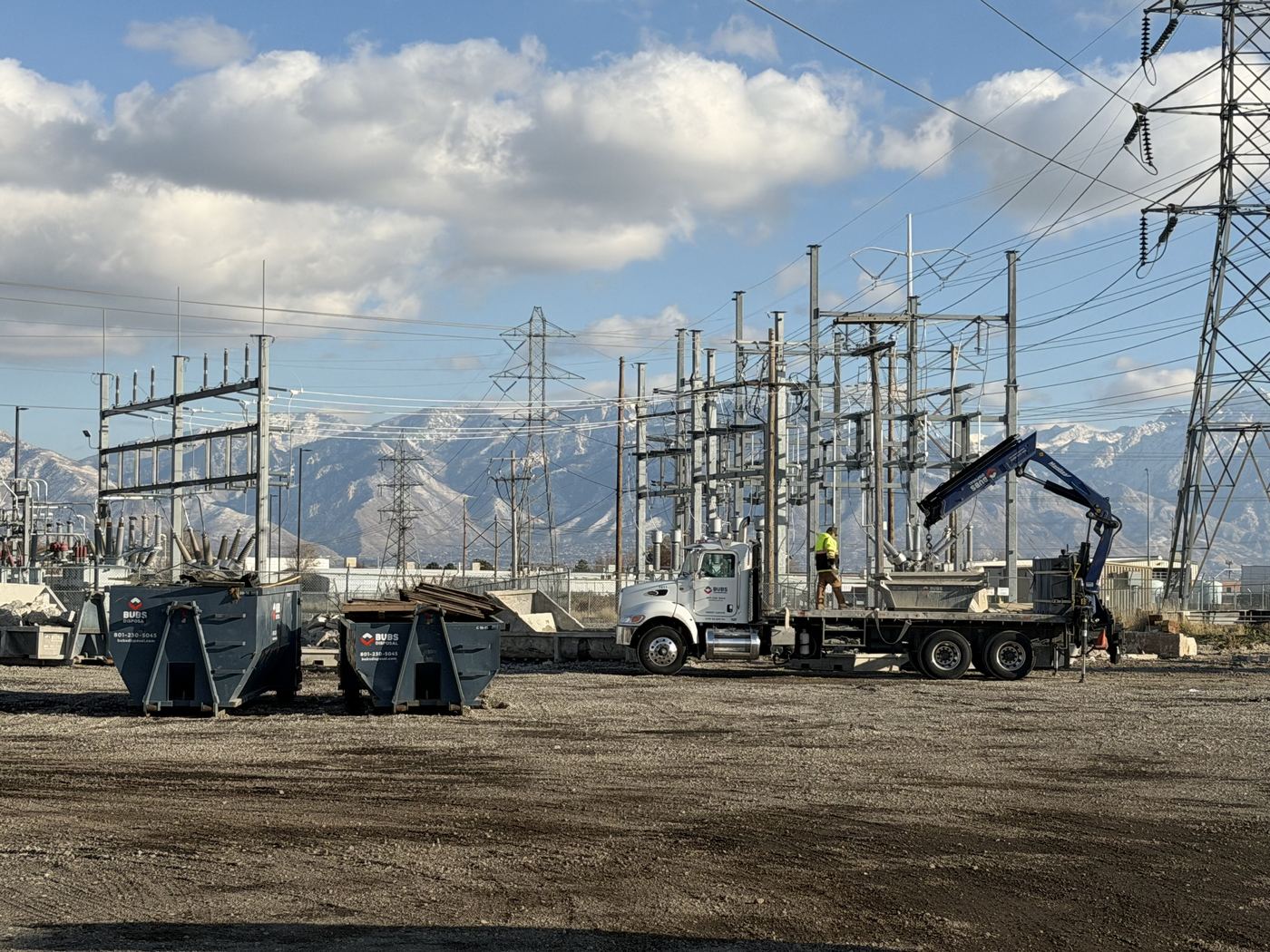 Bubs truck setting a washout pan with its crane, two dumpsters and mountains behind